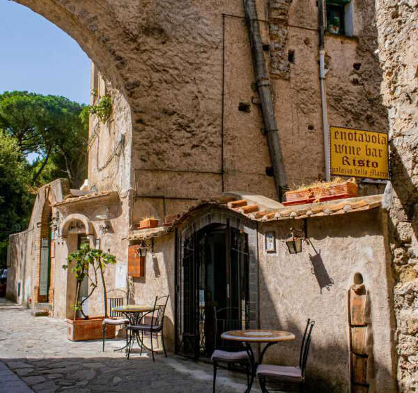 Ruelle typique de Ravello sur la Côte Amalfitaine avec une arche ancienne en pierre et une terrasse de restaurant.