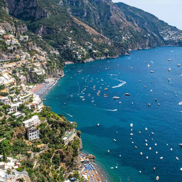 Vue panoramique aérienne de Positano sur la Côte Amalfitaine, montrant les maisons colorées à flanc de falaise et de nombreux bateaux naviguant sur une mer azur.