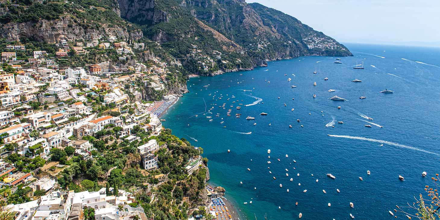Vue panoramique aérienne de Positano sur la Côte Amalfitaine, montrant les maisons colorées à flanc de falaise et de nombreux bateaux naviguant sur une mer azur.