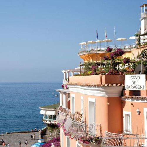 Façade de l'Hôtel Covo dei Saraceni à Positano avec terrasses, bougainvilliers et vue sur la mer.
