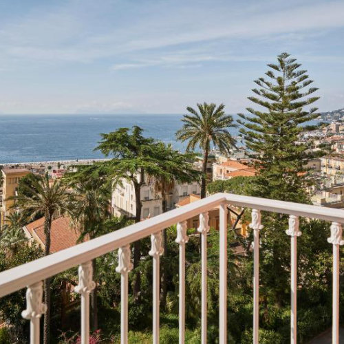 Panorama sur la végétation méditerranéenne et la mer bleue depuis un balcon à la rambarde blanche travaillée.