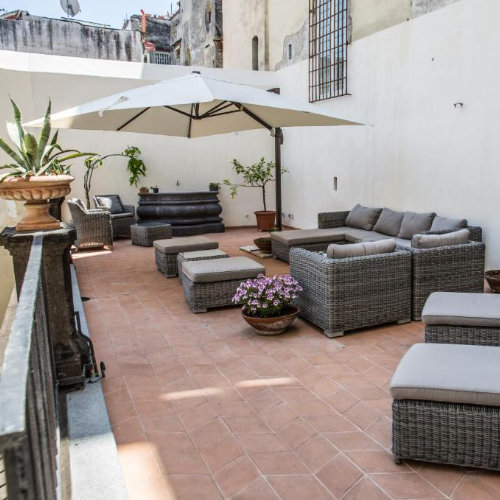 Terrasse d’hôtel à Naples avec salon extérieur, parasol et espace détente.