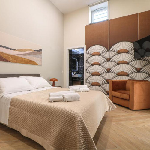 Chambre moderne à la Dimora Gioia à Pompéi avec un lit double, un fauteuil orange et un mur décoré de motifs en forme d'éventails.