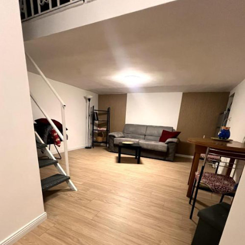 Espace de vie spacieux avec canapé gris, parquet au sol et escalier menant à une mezzanine.