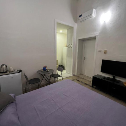 Chambre confortable avec grand lit double aux tons violets, coin café et télévision pour les invités.