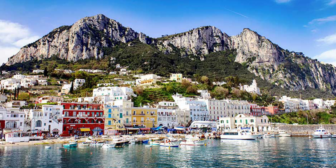 Maisons colorées et nombreux bateaux au port de Marina Grande à Capri, au pied de hautes falaises.
