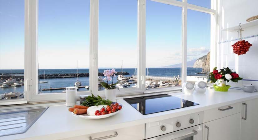 Cuisine lumineuse à Sorrente avec grande fenêtre, vue sur le port et produits frais.