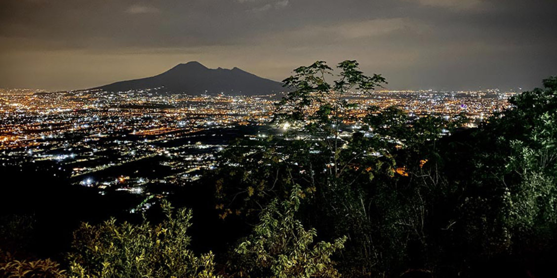Vue nocturne de Naples avec le Vésuve illuminé en arrière-plan.