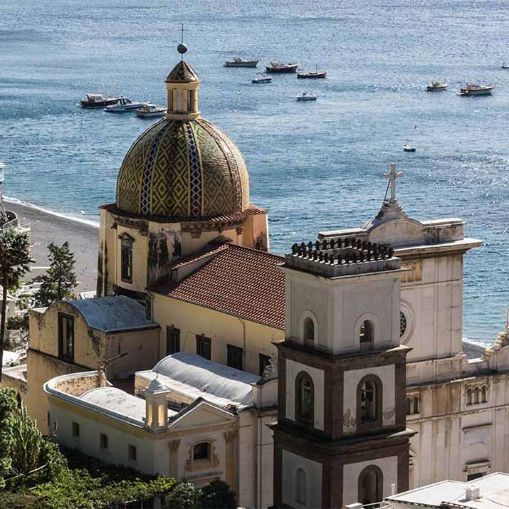 Dôme en majolique de l’église Santa Maria Assunta à Positano avec vue sur la mer et les bateaux.