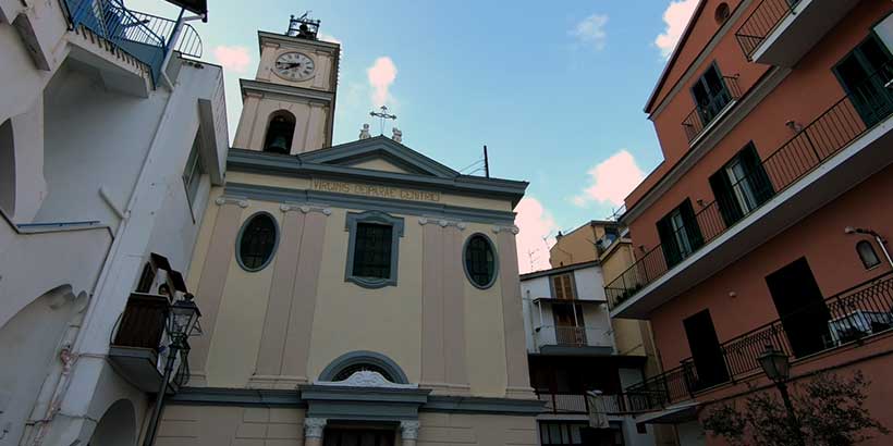Église Sant’Anna à Sorrente avec clocher, horloge et façades colorées autour.