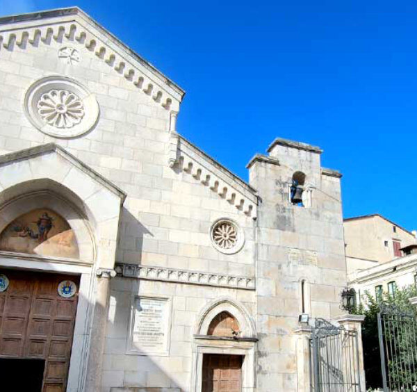 Église historique de Sorrente avec façade claire, rosace et clocher sous un ciel bleu.