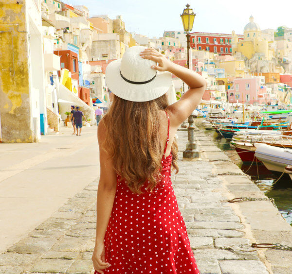 Une femme en robe rouge admirant le port coloré de Marina Corricella à Procida.