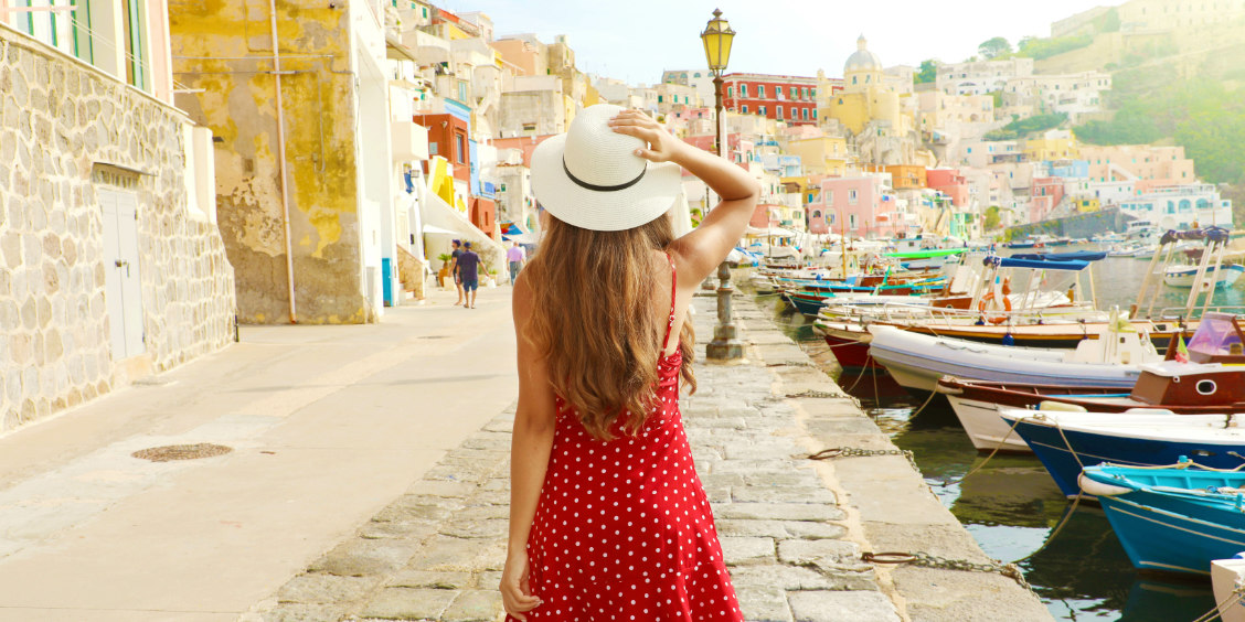 Une femme en robe rouge admirant le port coloré de Marina Corricella à Procida.