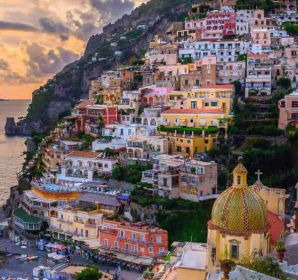 Positano au coucher du soleil avec maisons colorées, coupole de l’église et mer de la Côte Amalfitaine.