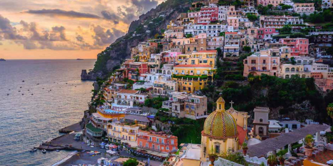 Positano au coucher du soleil avec maisons colorées, coupole de l’église et mer de la Côte Amalfitaine.