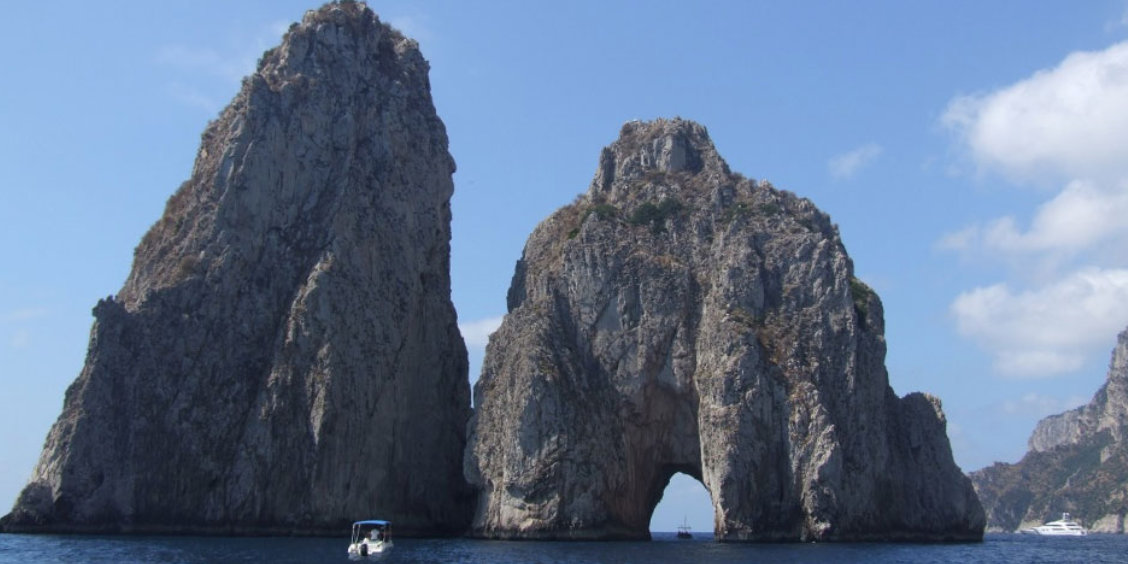 Les rochers Faraglioni de Capri émergeant de la mer bleue avec un bateau naviguant à proximité.