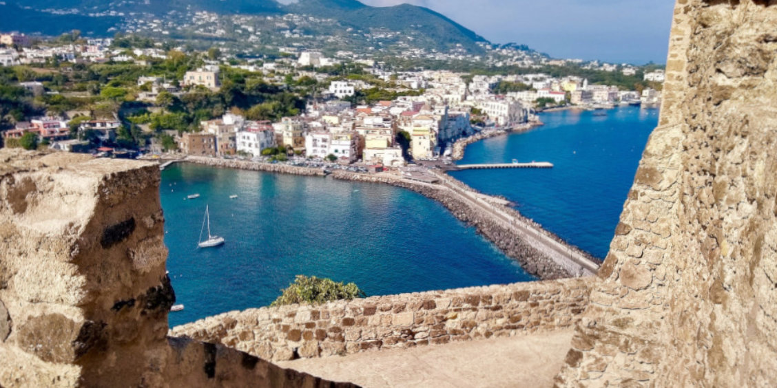 Vue sur Ischia depuis un château avec mer turquoise, village côtier et paysage méditerranéen.