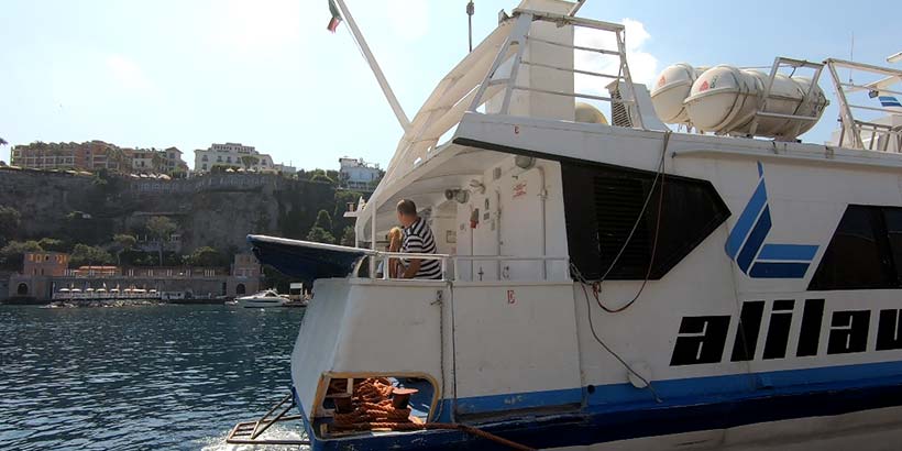 Ferry au départ de Naples avec passager à bord et vue sur la côte en arrière-plan.