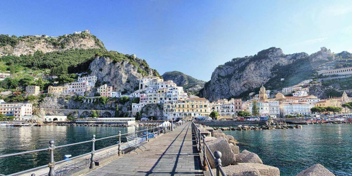 Port d’Amalfi avec embarcadère des ferries, mer et maisons au pied des falaises.