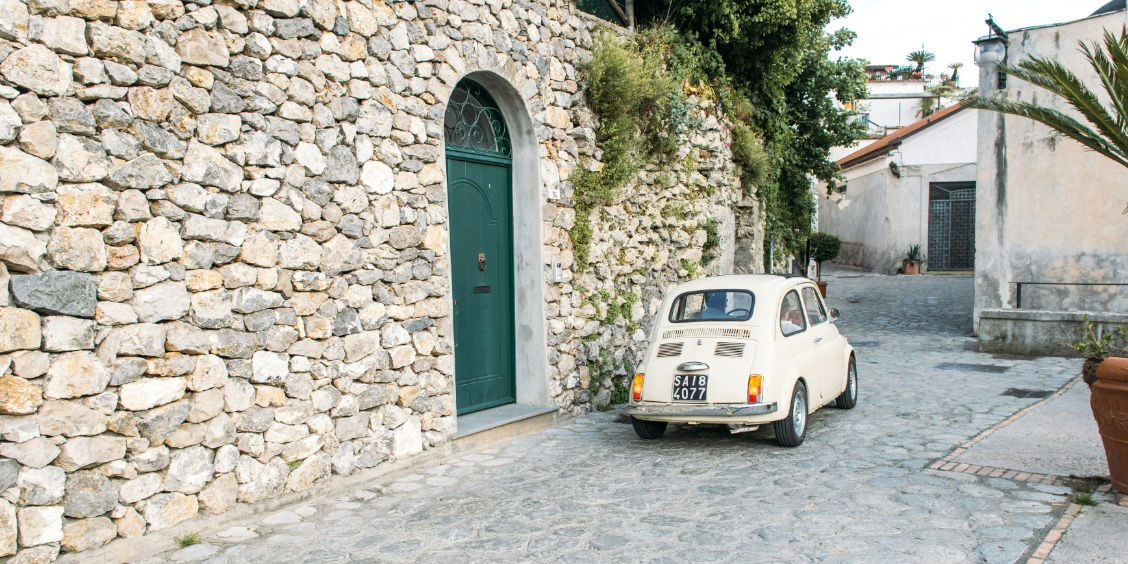 Voiture Fiat 500 d'époque stationnée le long d'un mur en pierre dans une ruelle pavée de Ravello.
