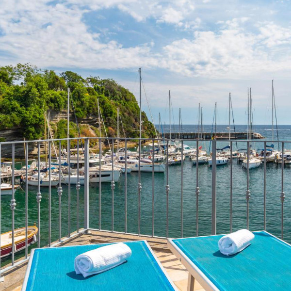 Terrasse avec chaises longues bleues surplombant le port de plaisance et ses voiliers.