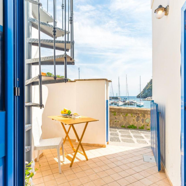 Petit coin extérieur avec table en bois et escalier en colimaçon offrant une vue sur le port.