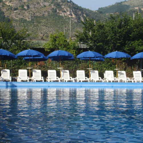 Piscine du Fiori d’Arancio à Sorrente avec transats, parasols bleus et montagnes.