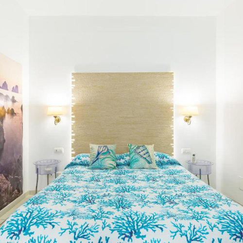 Chambre du Fortino Capri avec lit au motif corail bleu, tête de lit tressée et éclairage intégré.