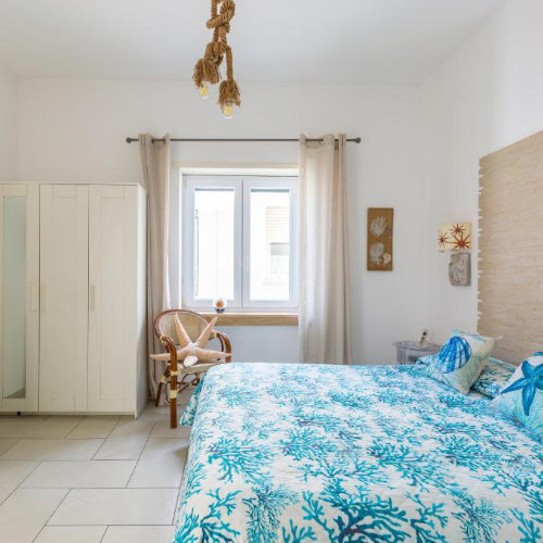 Vue de la chambre au Fortino Capri montrant le lit, une armoire blanche et une chaise avec coussin étoile de mer.