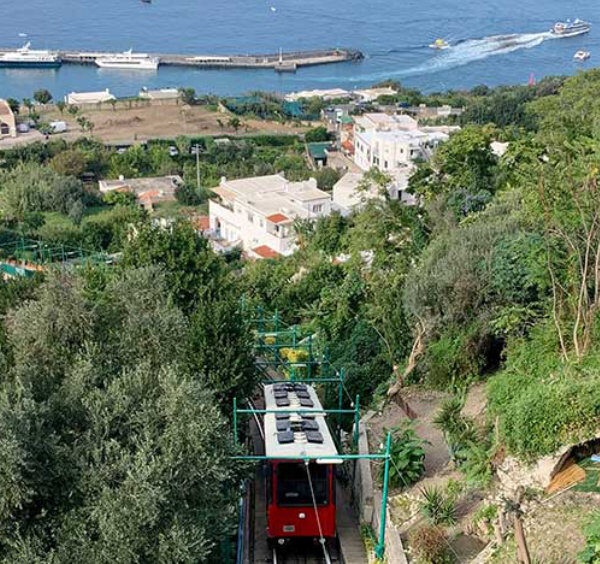 Funiculaire rouge de Capri montant vers le centre avec vue sur le port de Marina Grande.