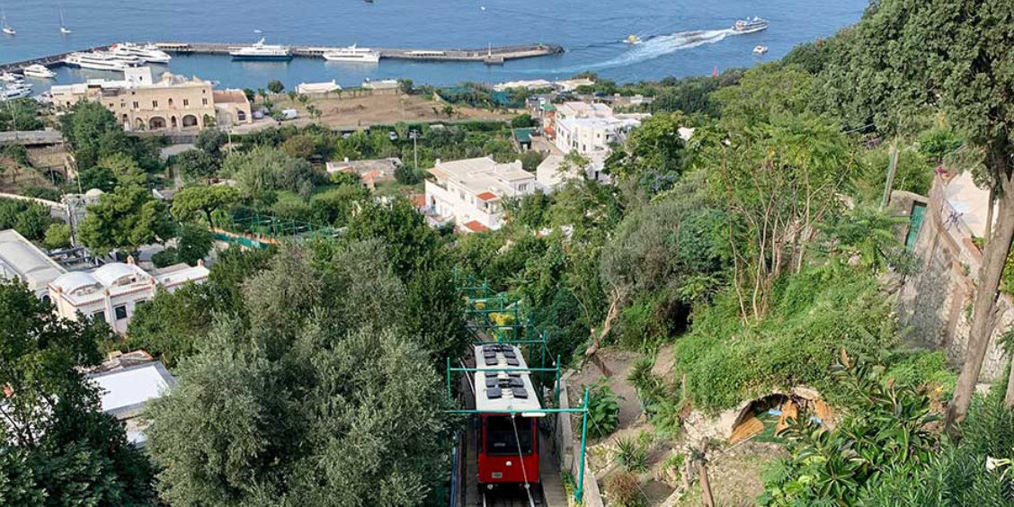 Funiculaire rouge de Capri montant vers le centre avec vue sur le port de Marina Grande.