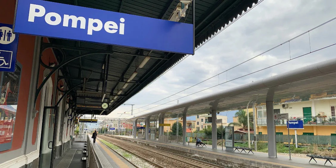 Gare de Pompei avec panneau bleu, quais et voies ferrées.