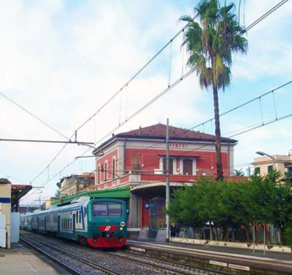 Train régional arrivant en gare de Pompei devant le bâtiment principal rouge sous un ciel clair.