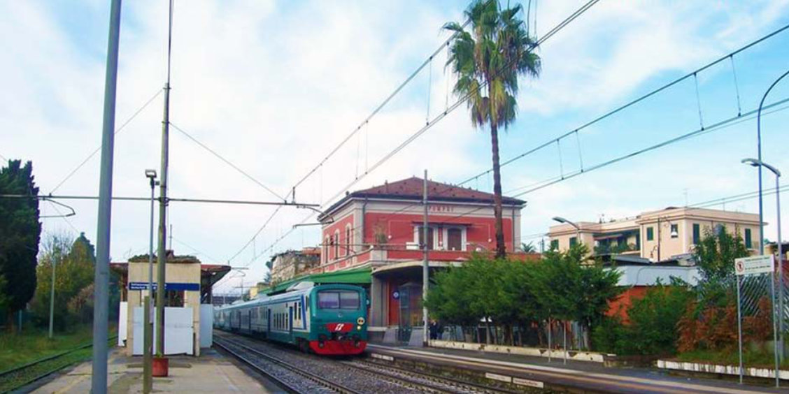 Train régional arrivant en gare de Pompei devant le bâtiment principal rouge sous un ciel clair.