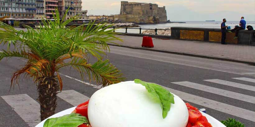 Plat de mozzarella fraîche avec tomates et basilic face au front de mer de Naples, avec le Castel dell’Ovo en arrière-plan.