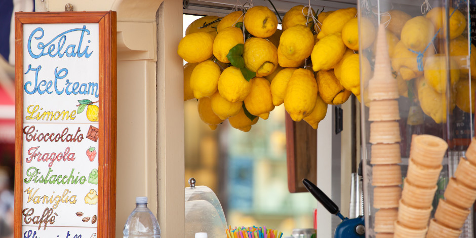 Étal de glacier à Capri avec un menu artisanal, des citrons jaunes suspendus et des piles de cônes en gaufrette.