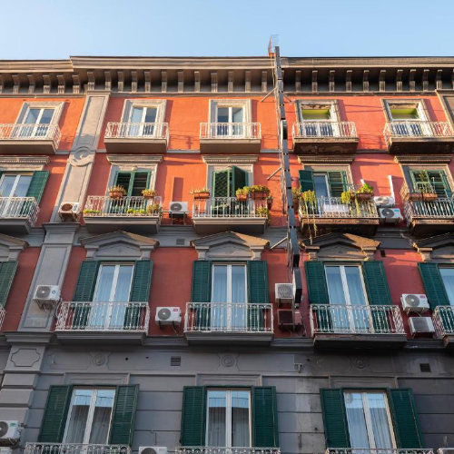 Façade extérieure du Grand Hotel Europa à Naples montrant les étages supérieurs rouges, les balcons et les volets verts.