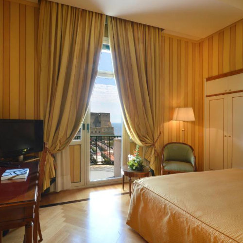 Chambre élégante du Grand Hotel Vesuvio à Naples avec balcon et vue sur le Castel dell’Ovo.