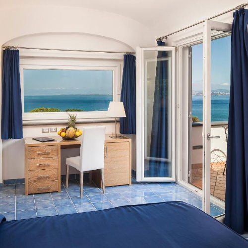 Chambre lumineuse avec balcon et vue panoramique sur la mer au Grifo Hotel.