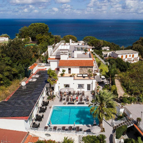 Vue aérienne de la piscine et de l'architecture du Grifo Hotel surplombant la mer.