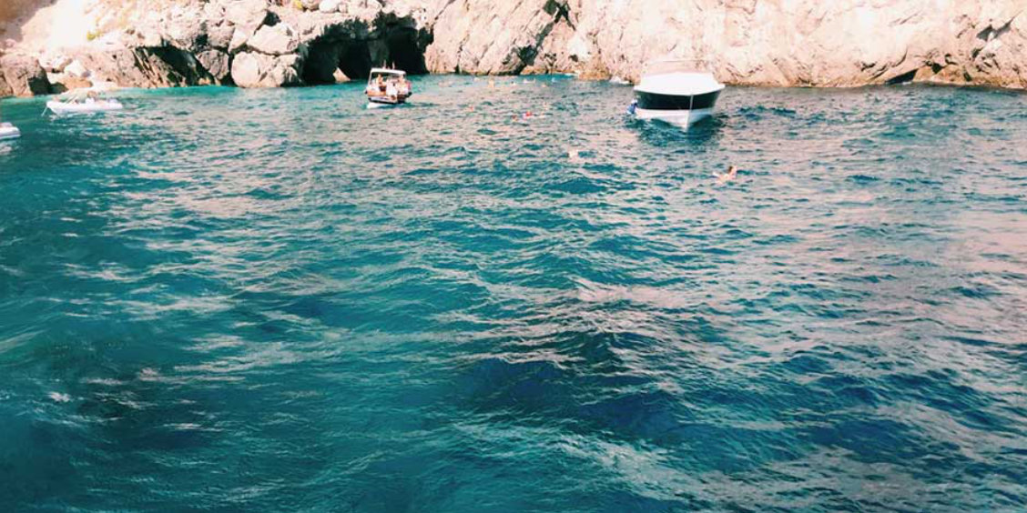 Eaux turquoises et falaises de la Grotte Verte à Capri avec des bateaux et des baigneurs.