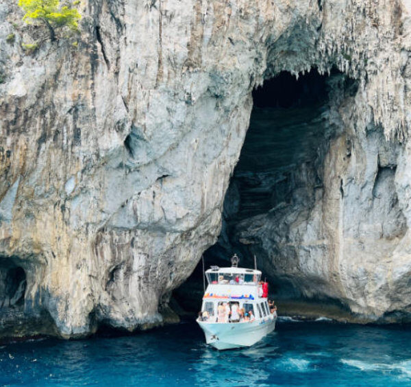 Bateau de tourisme à l'entrée de la Grotte Blanche à Capri entouré de hautes falaises calcaires.