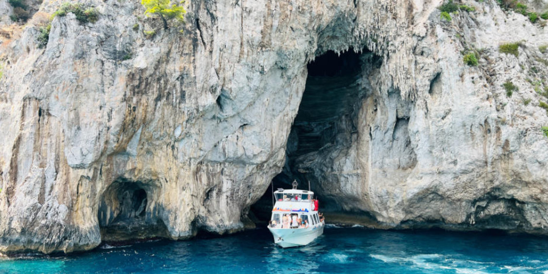 Bateau de tourisme à l'entrée de la Grotte Blanche à Capri entouré de hautes falaises calcaires.