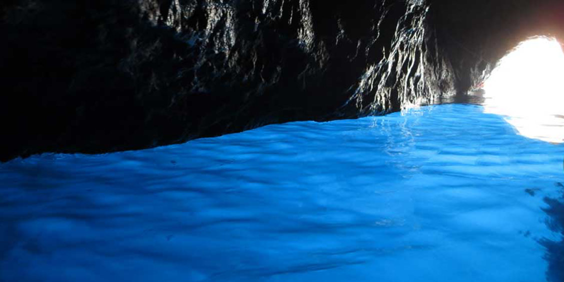 Intérieur de la Grotta Azzurra à Capri montrant l'eau luminescente bleu électrique sous les parois rocheuses sombres.