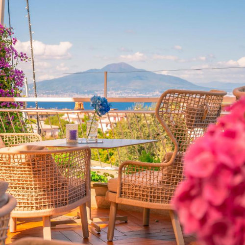Terrasse du Hilton Sorrento Palace avec fauteuils, fleurs et vue sur le Vésuve.