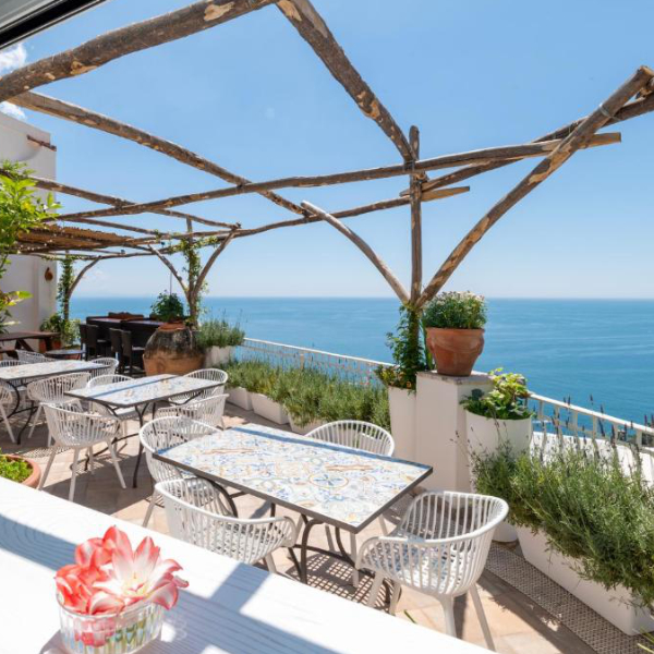 Terrasse du Hostel Brikette à Positano avec tables et vue panoramique sur la mer.