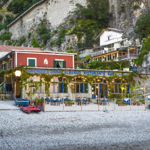 Façade rouge de l'Hôtel Alfonso a Mare et sa terrasse sur la plage de galets à Praiano.