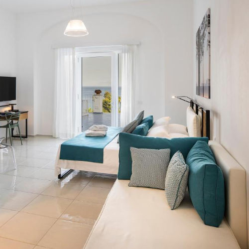 Chambre moderne aux tons blancs et turquoise avec accès au balcon et vue mer.
