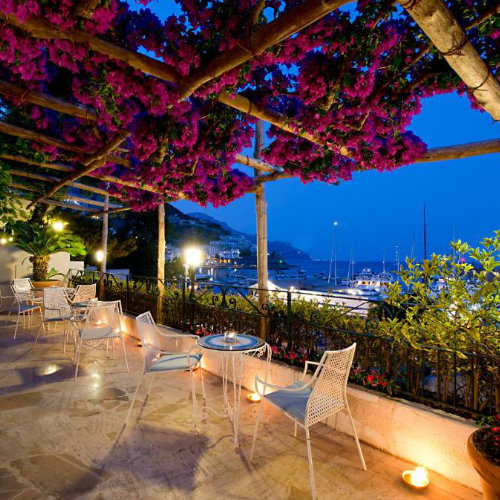 Terrasse fleurie de l’Hotel Aurora à Amalfi avec vue sur le port le soir.