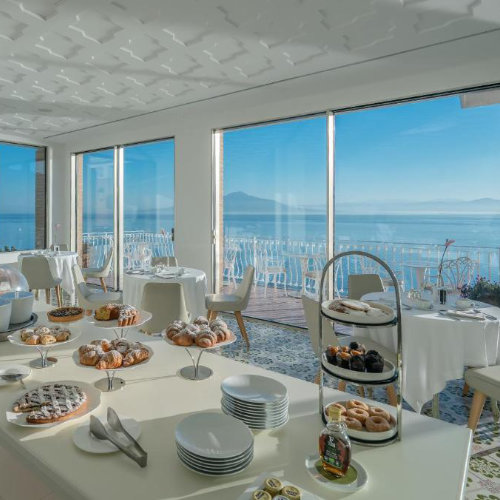 Salle du petit-déjeuner de l’Hotel Belair à Sorrente avec buffet et grandes baies vitrées sur le golfe.